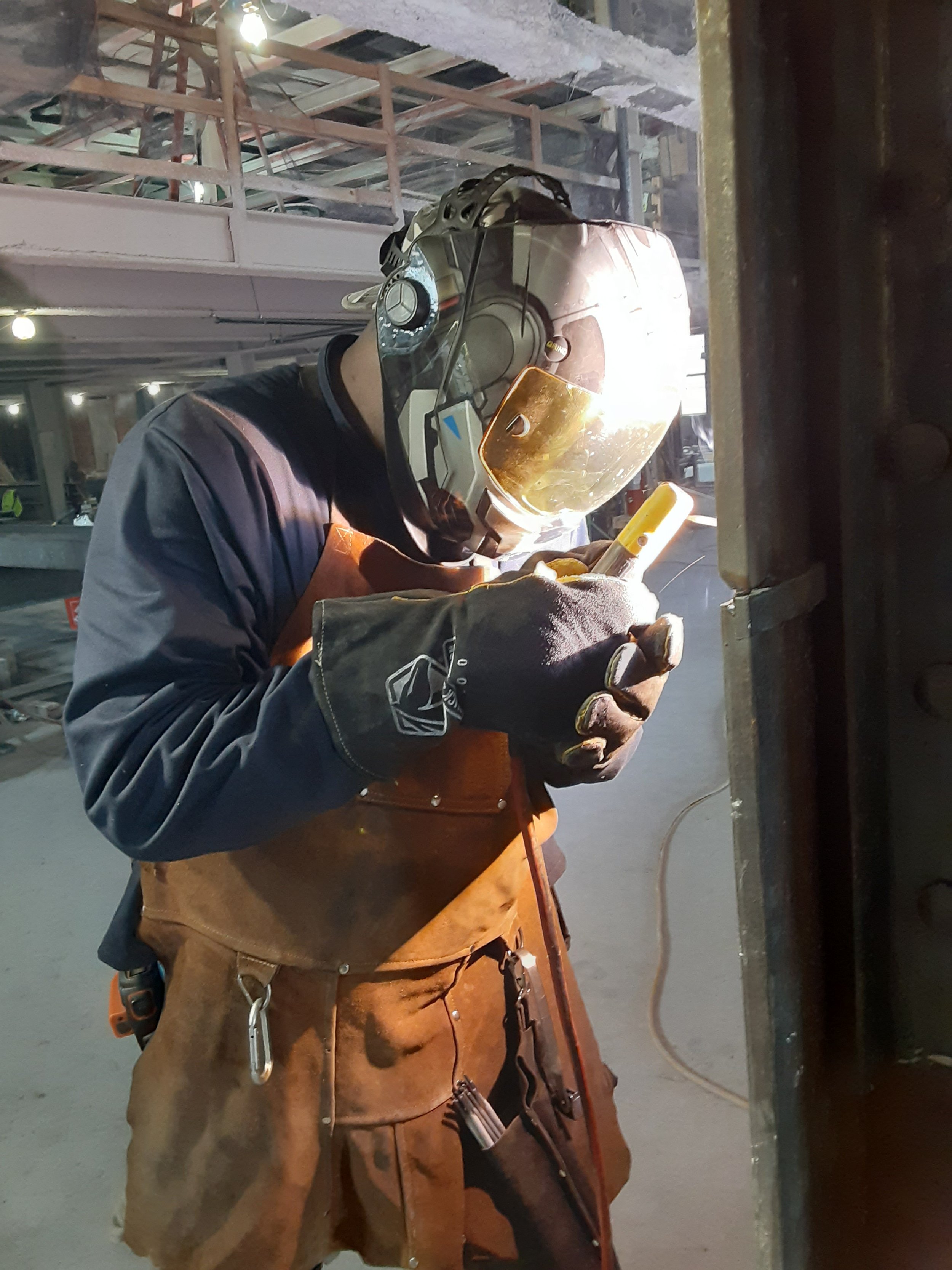 A welder wearing a helmet and protective gear working in an industrial setting.
