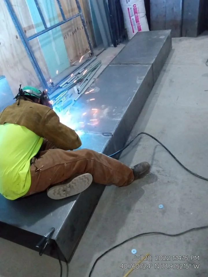 Person welding metal in workshop, wearing protective gear.
