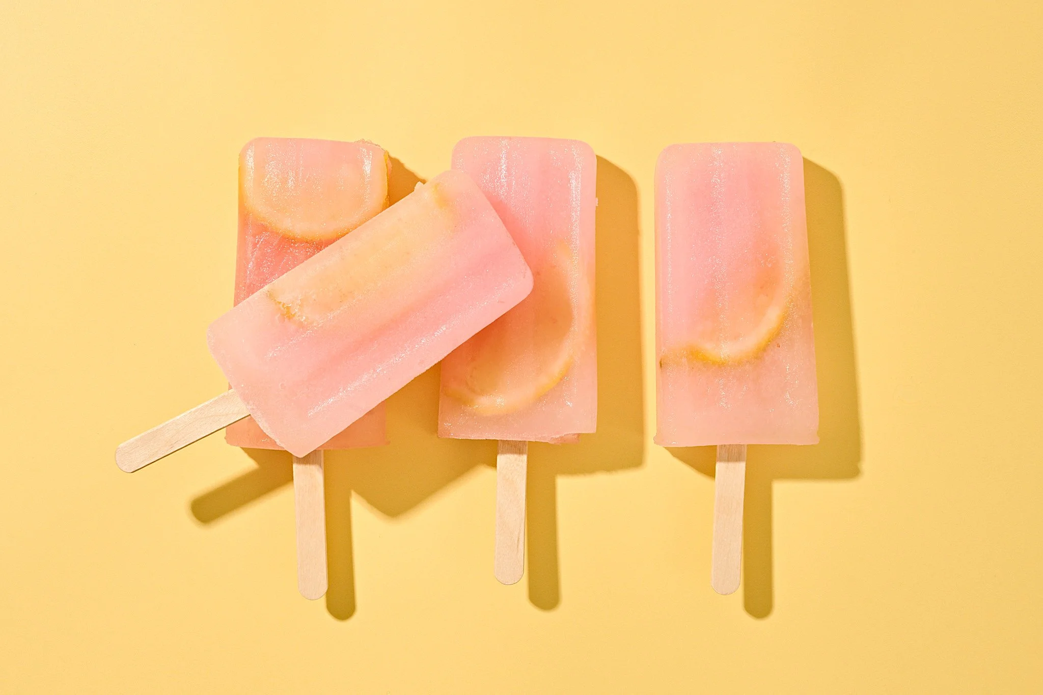 Three pink popsicles with lemon slices on a yellow background. commercial food photography product photographer freelance consumer brand 