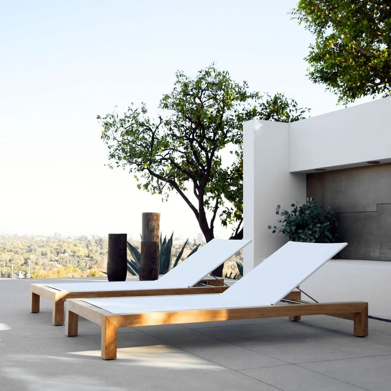 A modern outdoor patio with two white lounge chairs, black vases, green plants, a tree, and a scenic view in the background.