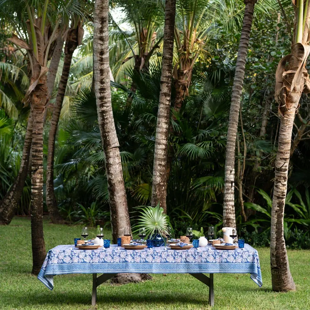 An outdoor table set for a meal in a tropical garden with tall palm trees and lush greenery.
