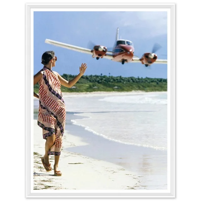 A person standing on a beach, waving at a small aircraft flying close overhead.