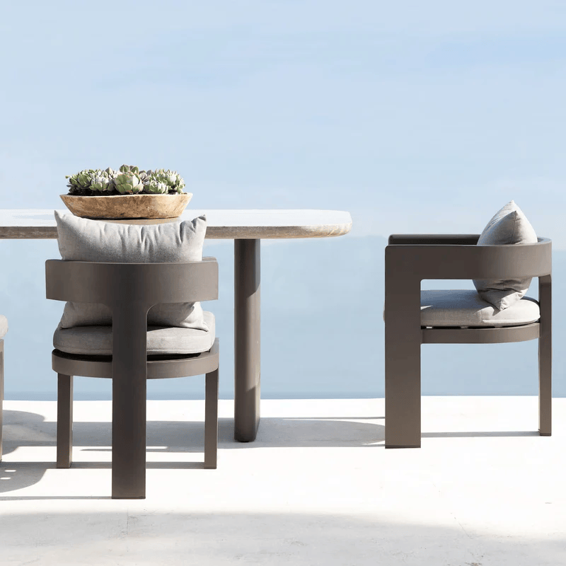 Outdoor patio table with cushions and a potted succulent plant against a light blue sky.