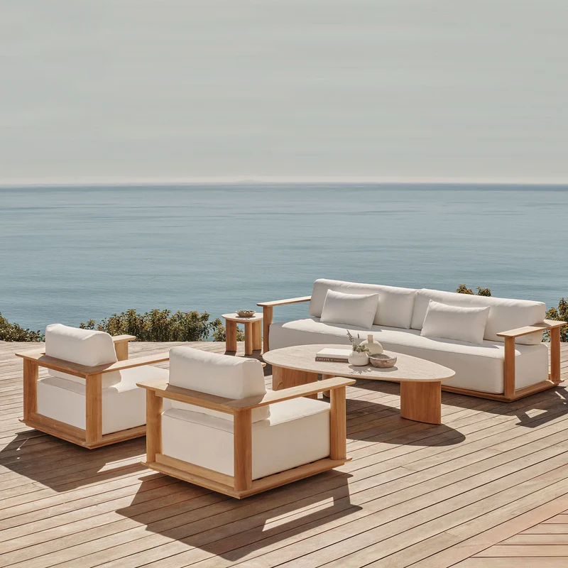 Outdoor seating area with white cushions, wooden furniture, and a view of the ocean and clear sky.