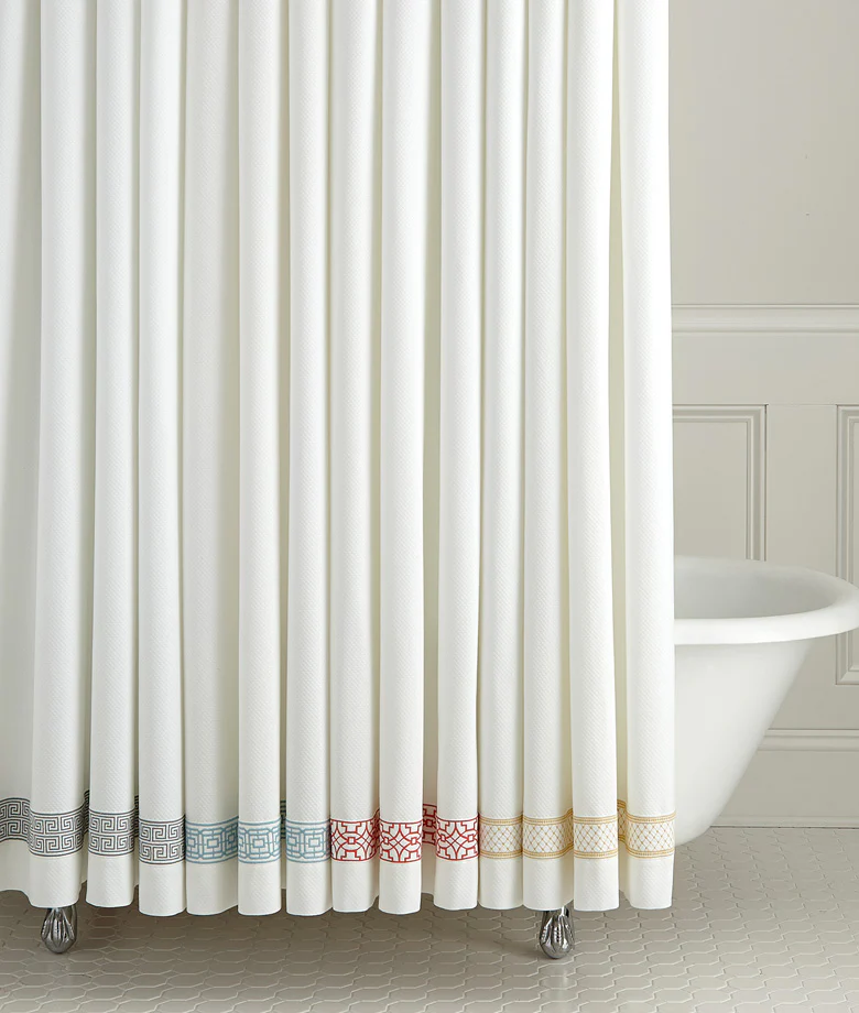 White curtain with geometric border patterns in black, blue, red, and gold, partially revealing a clawfoot bathtub in a bathroom.