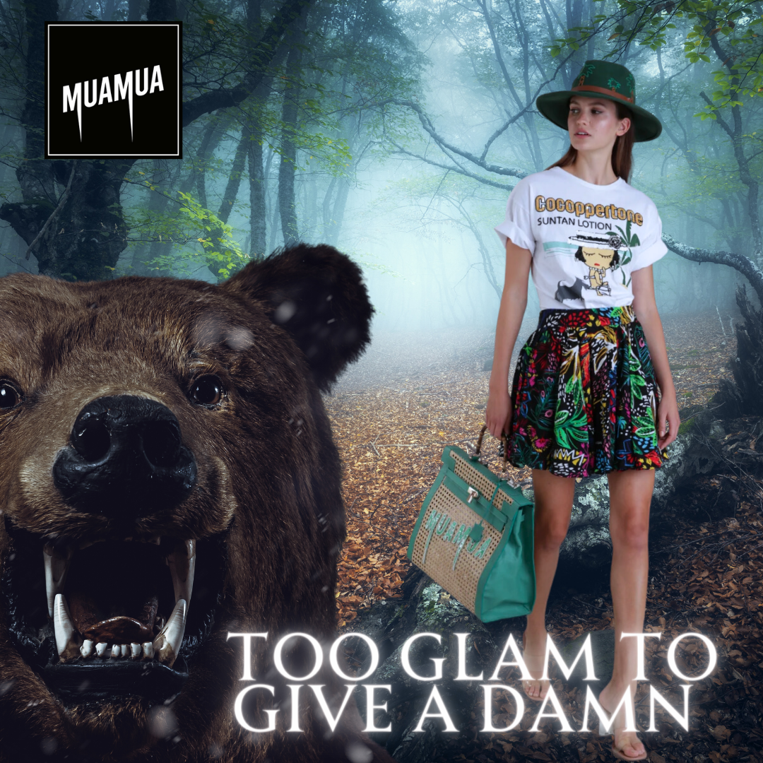 Donna con cappello e gonna colorata, che tiene una borsa sulla spiaggia, con un orso del sesso femminile che svetta accanto a lei in un bosco. Testo in inglese: "TOO GLAM TO GIVE A DAMN" e un logo in alto a sinistra con la scritta MUAMUA.