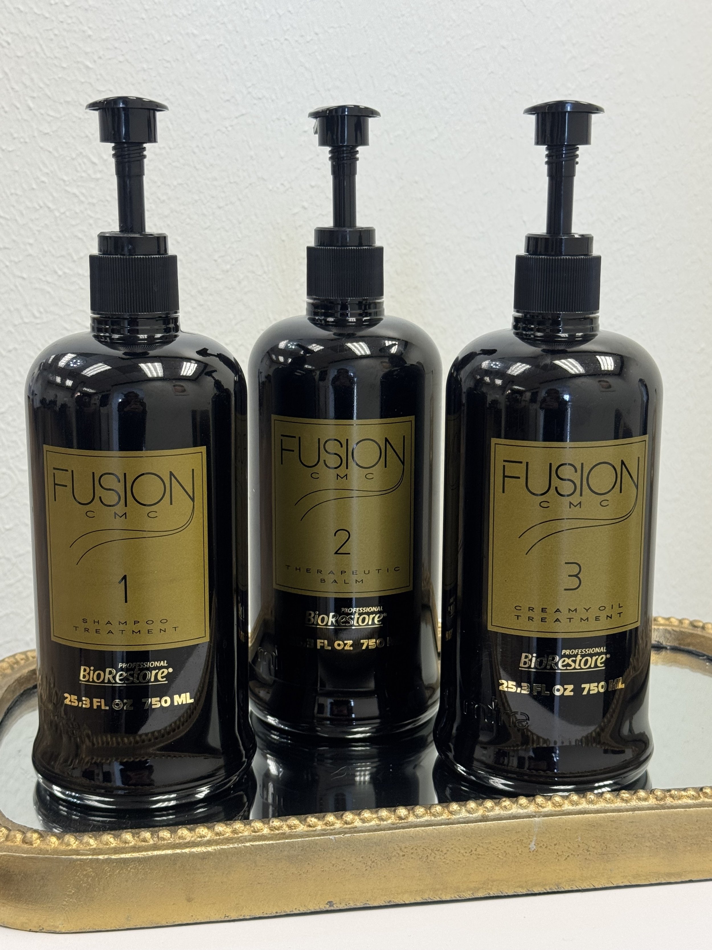 A woman with long, wavy blonde hair, wearing a black lace top and a black headband, is reaching for hair care products on a shelf. The products include bottles and tubes labeled with varying colors and texts.