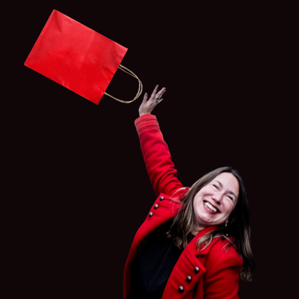 Person in red coat joyfully holding a flying red shopping bag against a dark background.