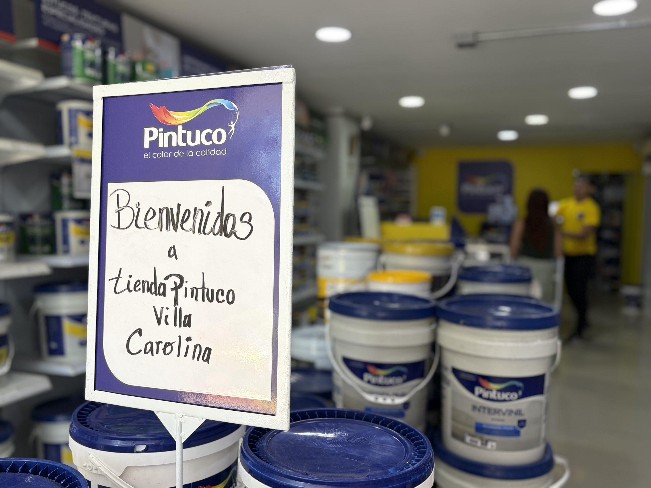Sección de pinturas en una tienda, con un cartel que dice 'Bienvenidos a tiendo Pintuco Villa Carolina'.
