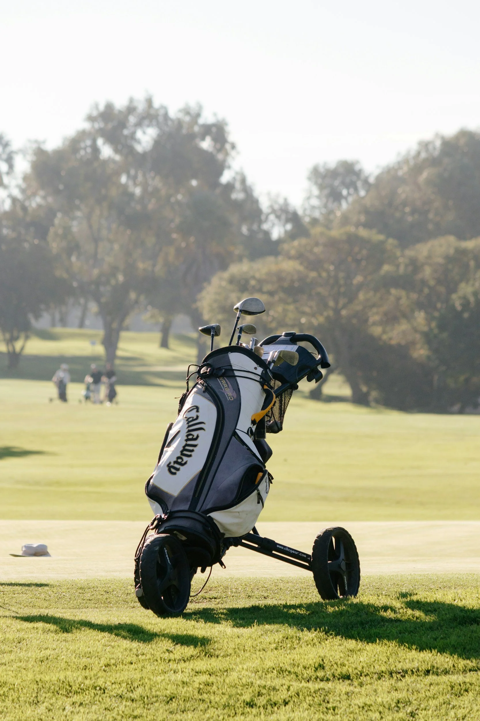 A Callaway golf bag on a golf course with trees and people in the background.