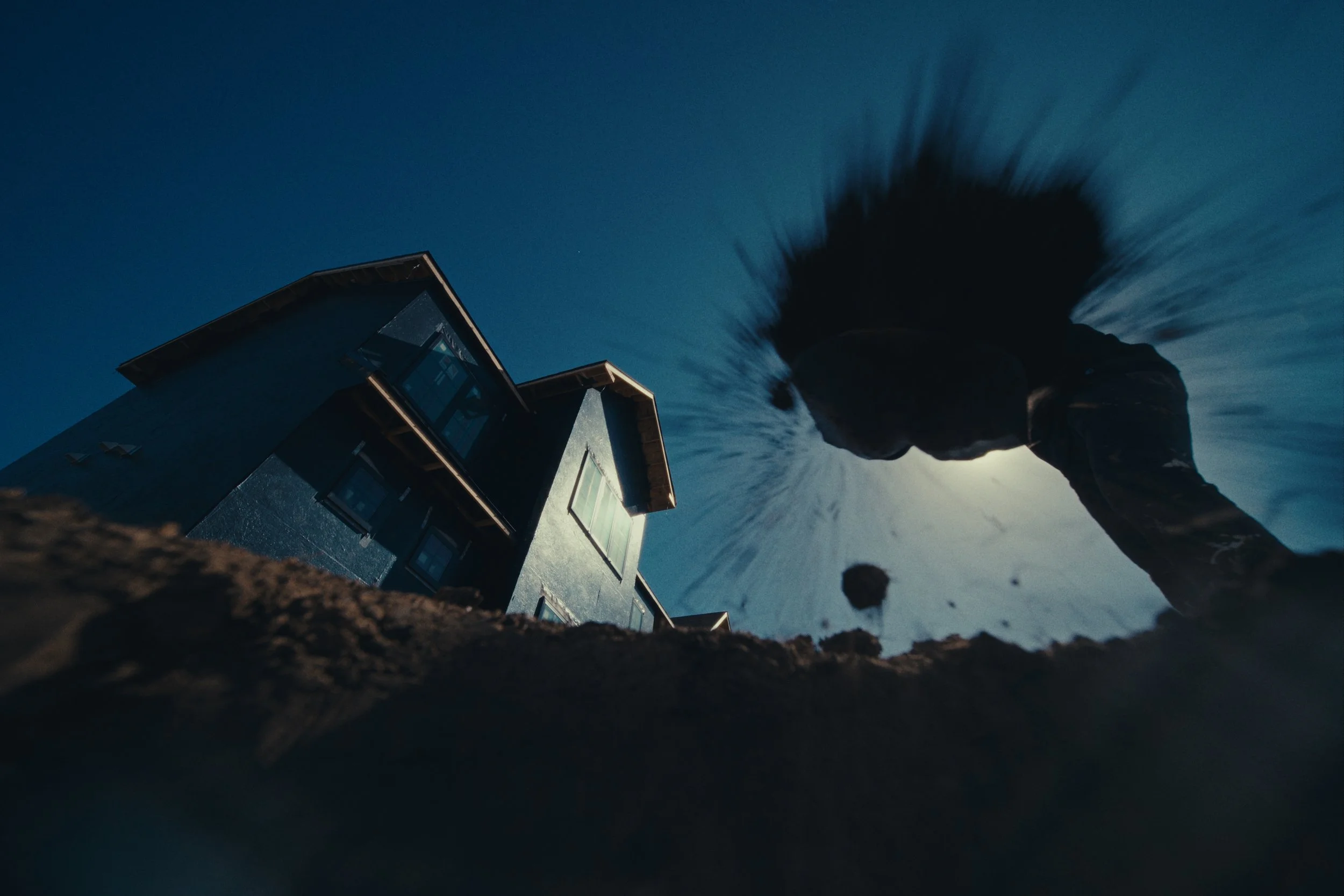 Person with long hair in motion, seen from below, with a house and blue sky in the background.