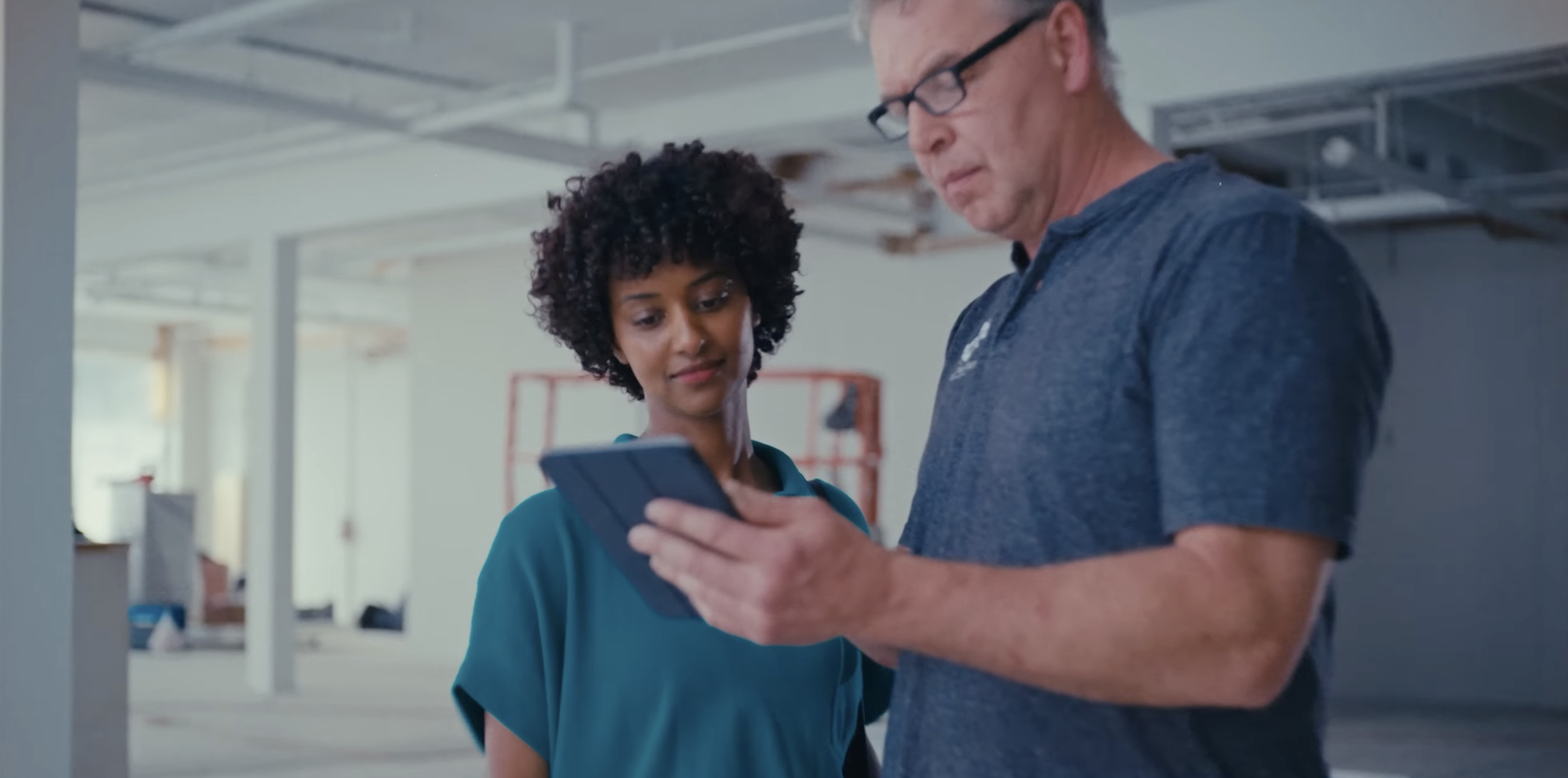 A man and woman looking at a smartphone together in an indoor construction or renovation site.