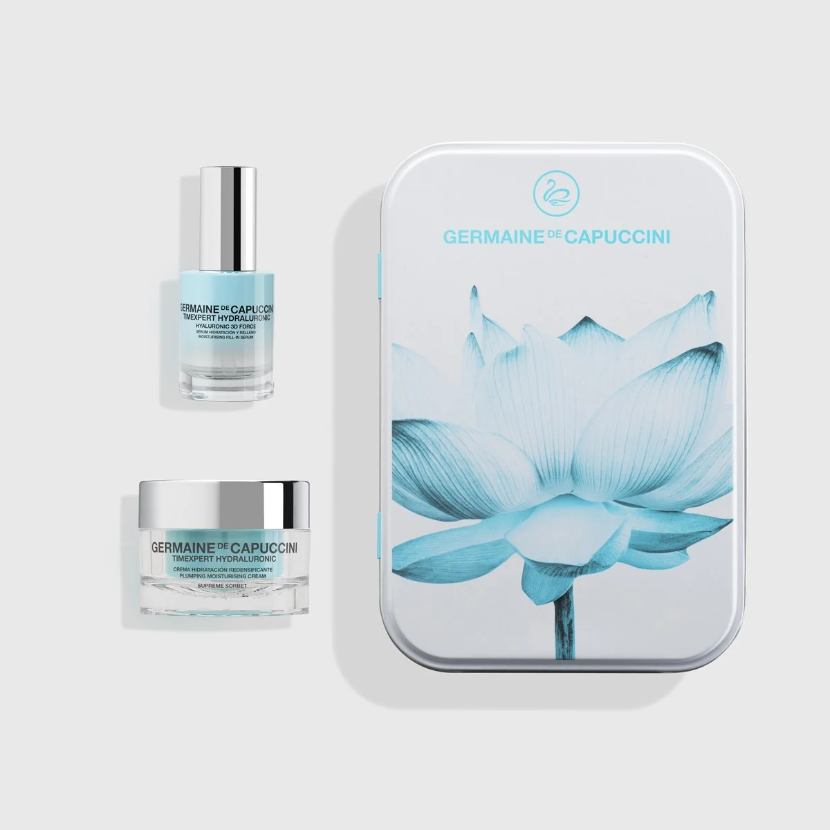 Set de productos de cuidado facial de la marca Germaine de Capuccini, incluye un frasco de suero y una crema en envases de color azul y plata, acompañado de una caja decorada con una ilustración de un loto en tonos azules.