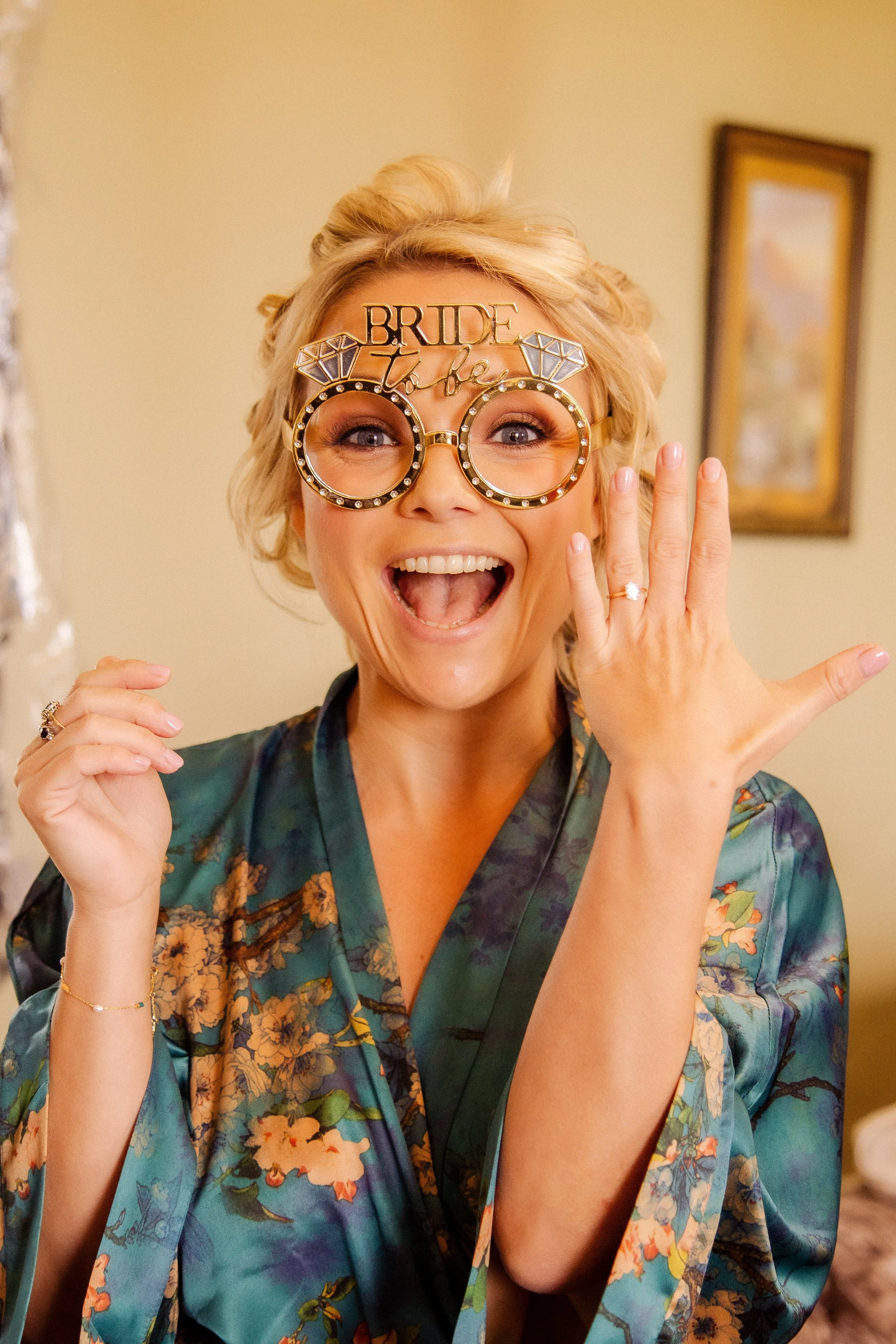 Woman in floral kimono celebrating her wedding with jewelry, fun glasses, and a 'bride to be' accessory.