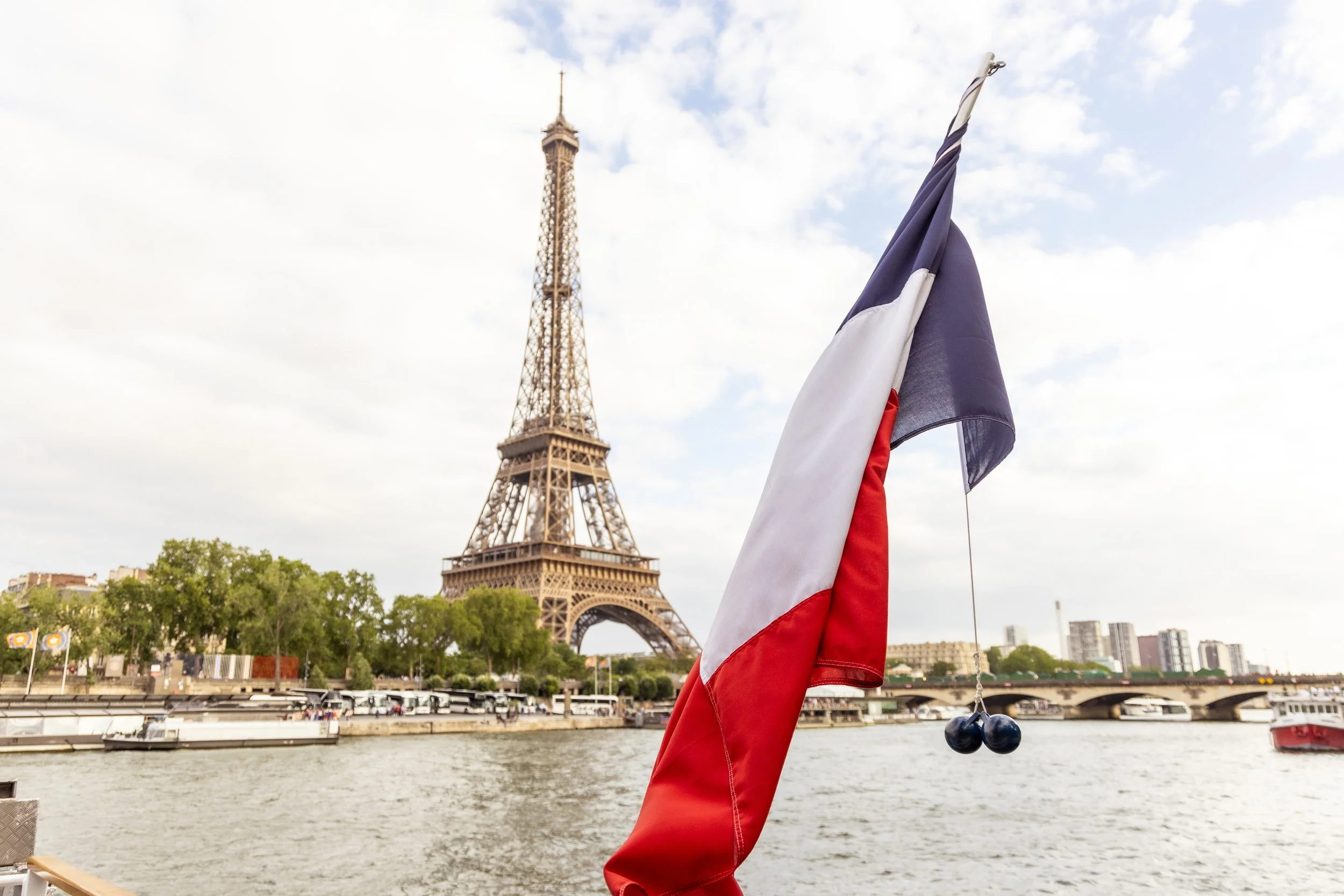 French flag on a boat with the Eiffel Tower in the background on a cloudy day.
