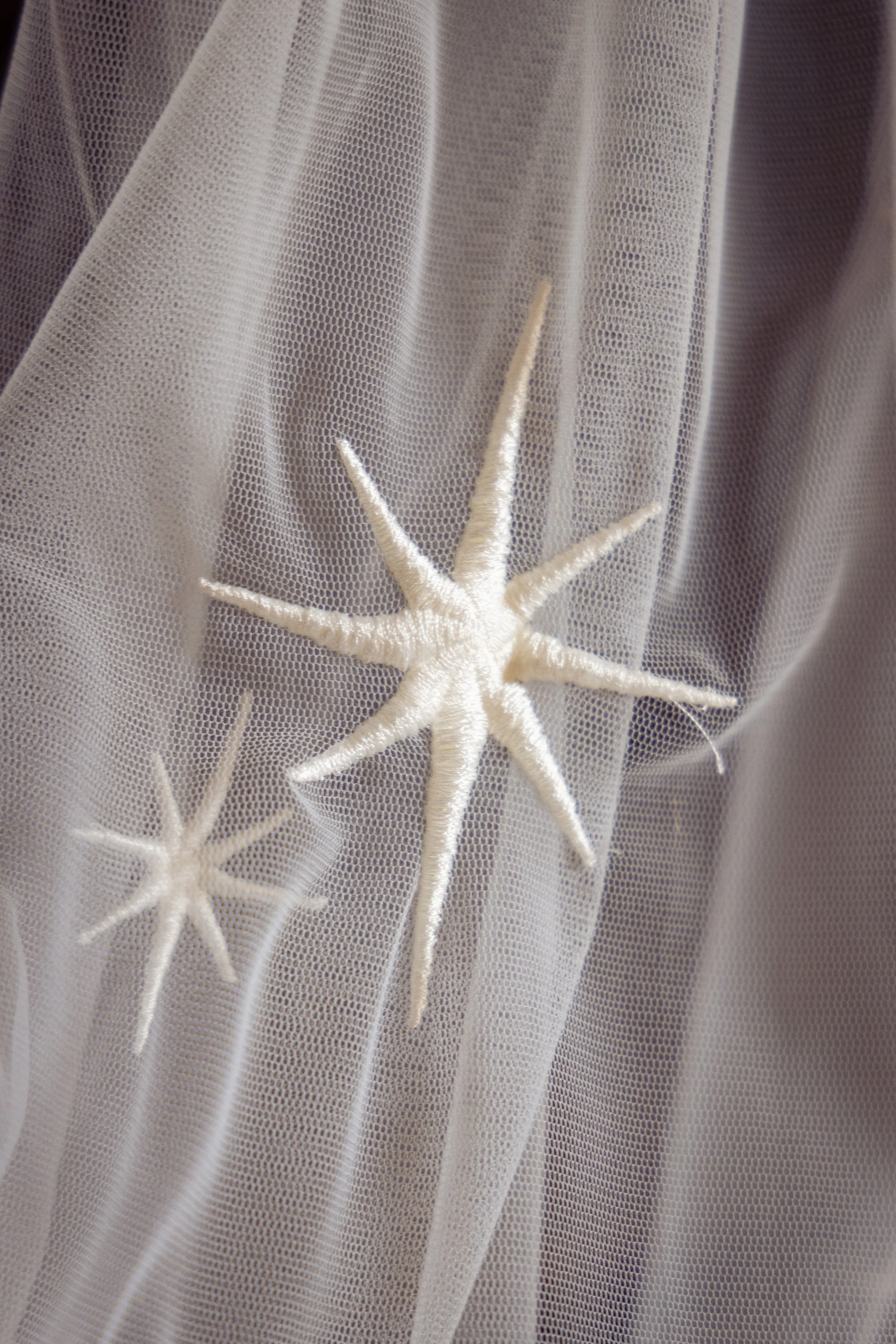 Close-up of white embroidered starfish designs on sheer white fabric with fine dot pattern.