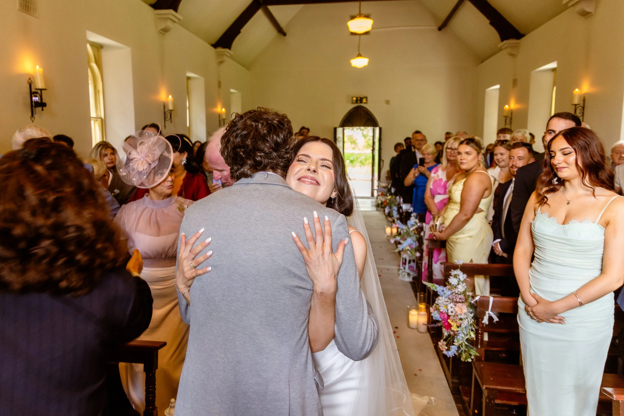 A bride is hugging a man during a wedding ceremony inside a church with guests watching and smiling.