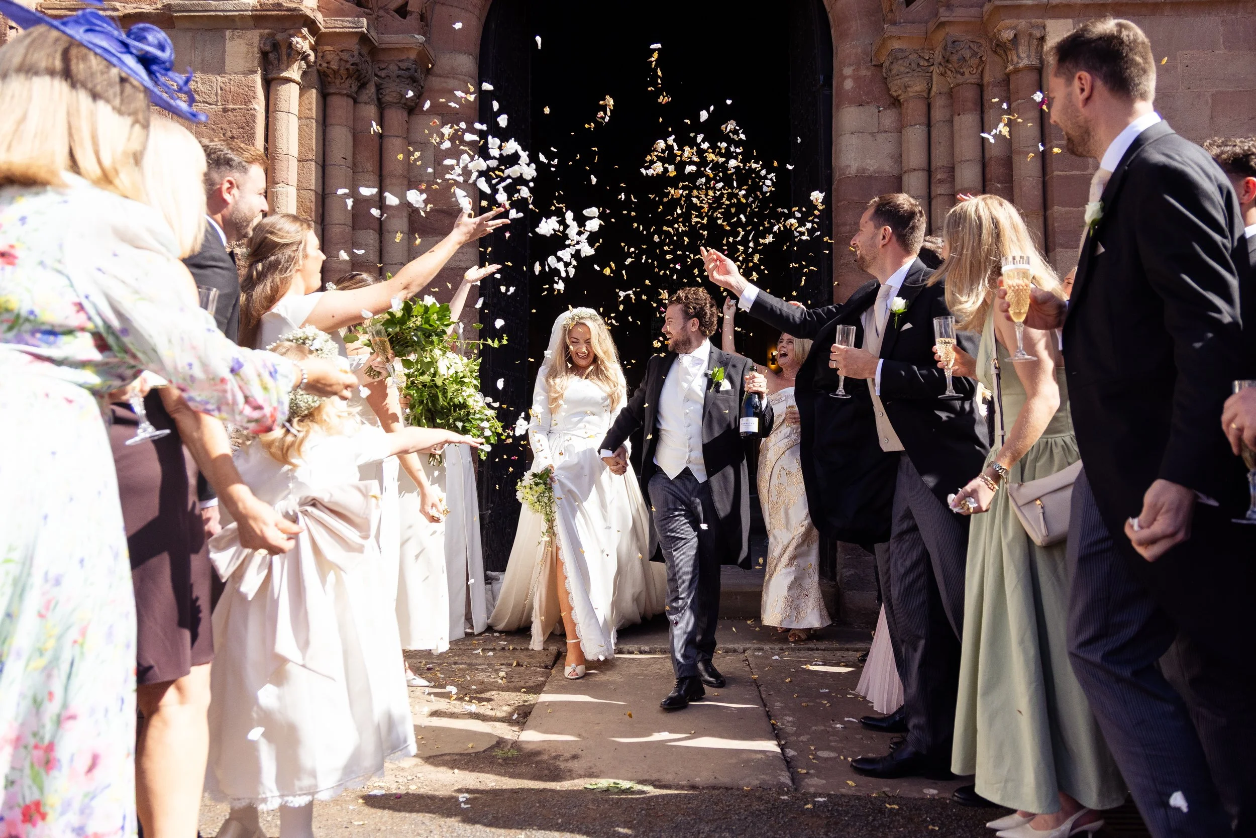 Celebrating a wedding outside a church with people throwing flower petals and confetti, with the bride and groom smiling in the center.