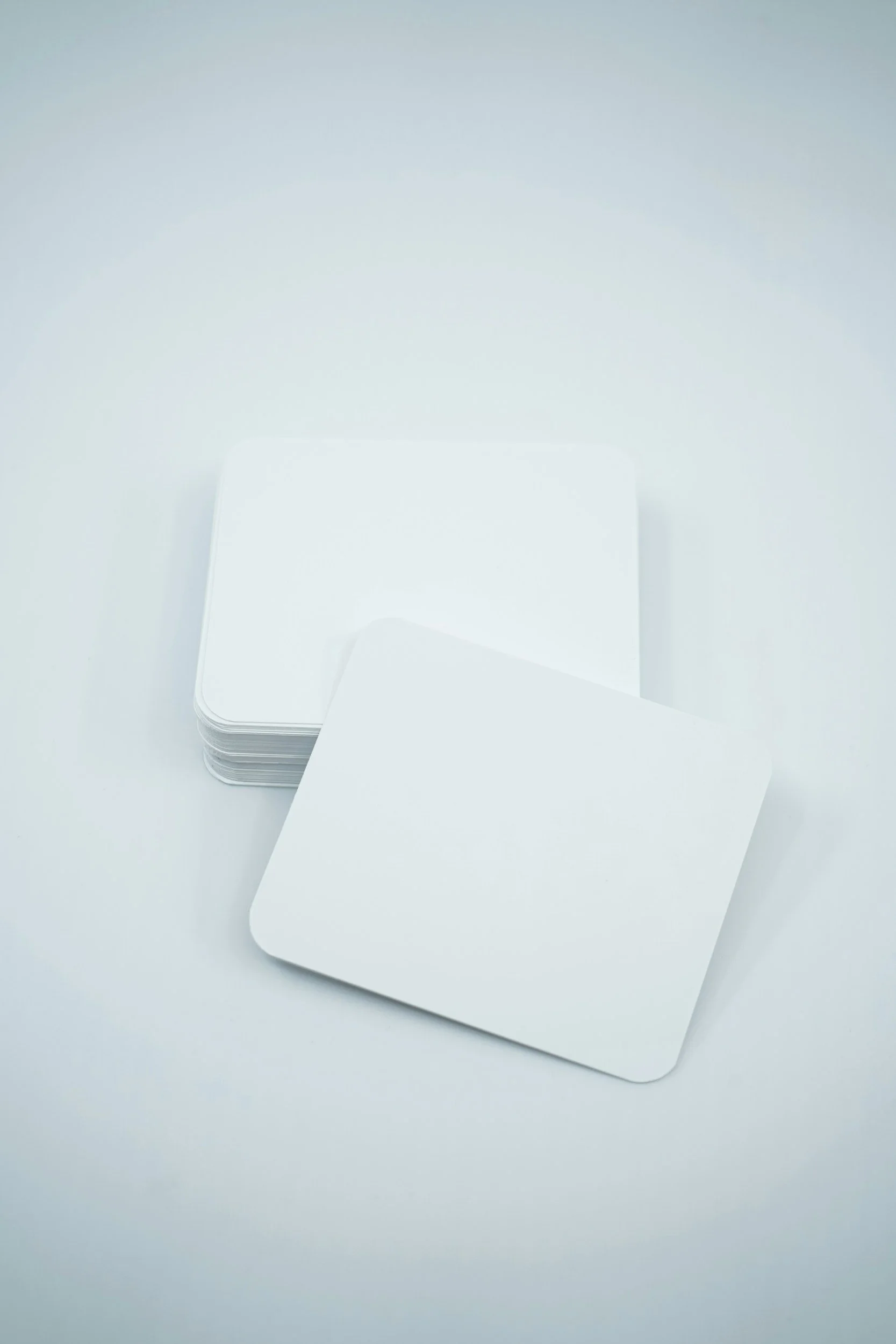 A stack of blank white square cards on a light background, with one card slightly separated from the stack.