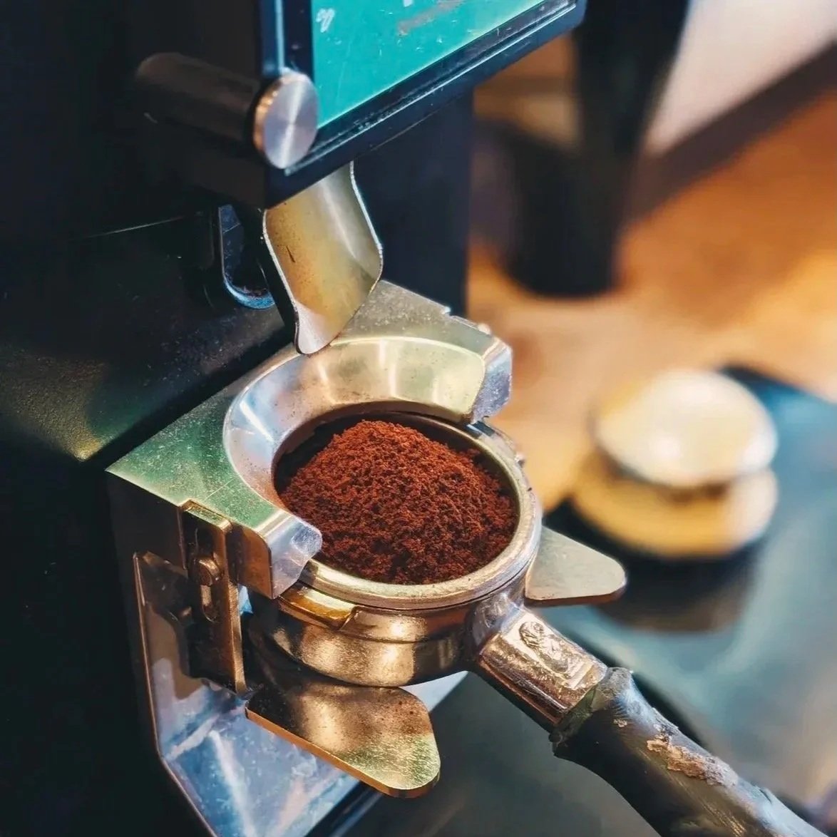 Close-up of a portafilter filled with ground coffee attached to a coffee machine, ready for brewing.