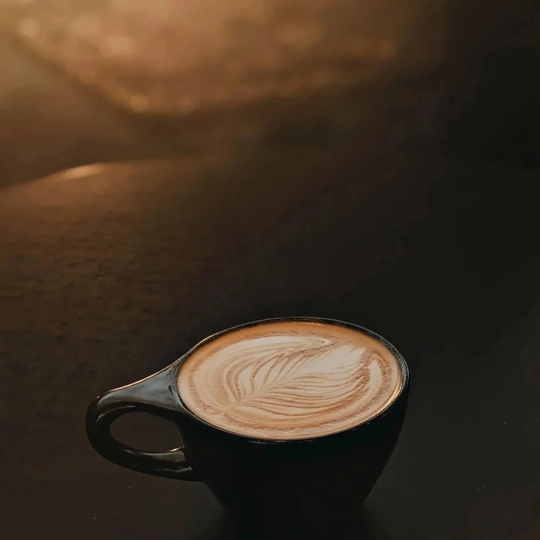 A black mug filled with a latte showing latte art, sitting on a dark surface with a dark background.