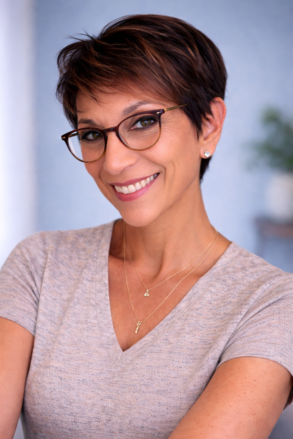 Woman with short hair smiling indoors, wearing earrings and a necklace.
