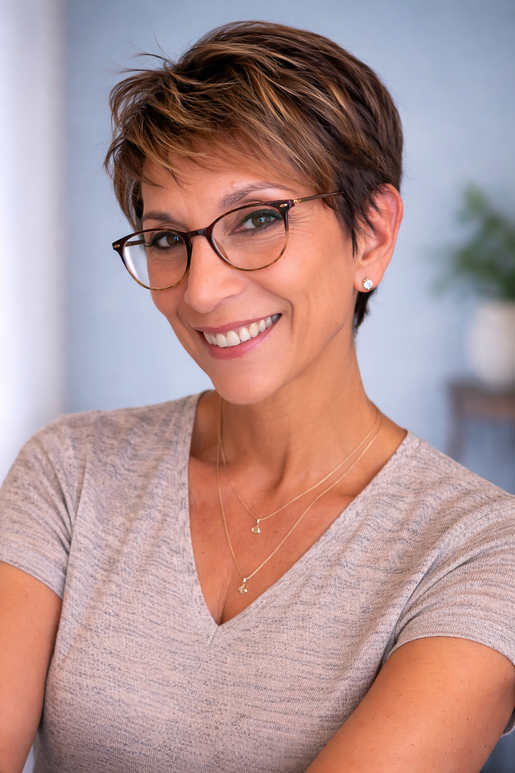 Woman with short hair smiling indoors, wearing earrings and a necklace.