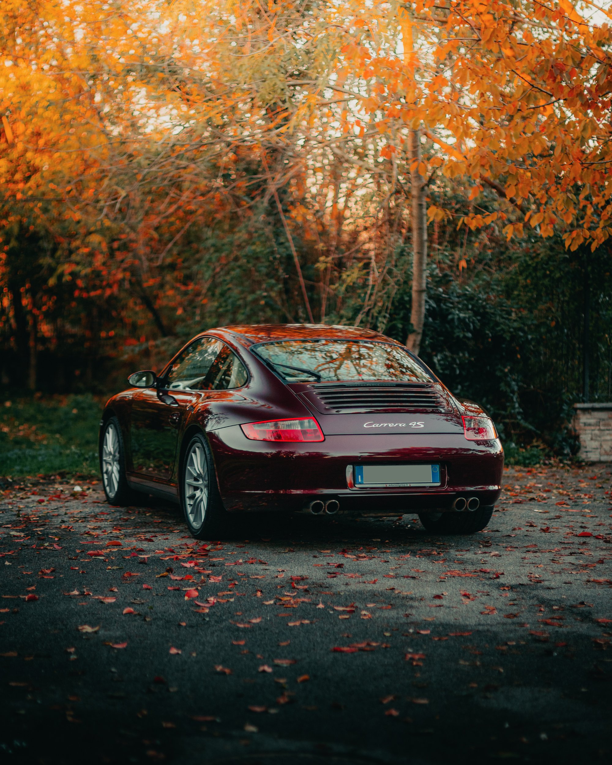 Auto sportiva rossa in un ambiente autunnale con foglie gialle e arancioni sullo sfondo.