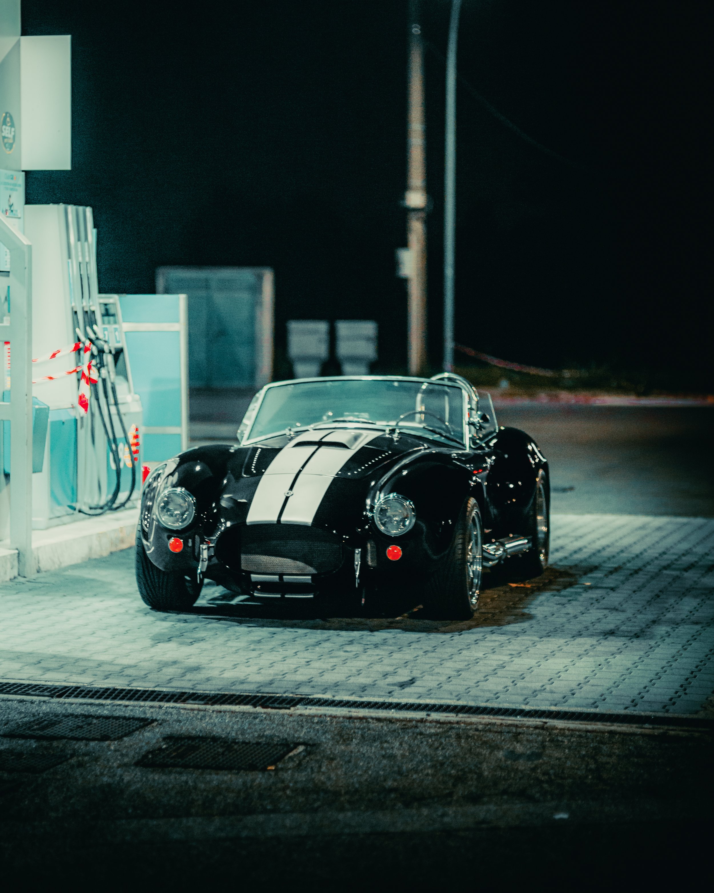 Auto sportiva nera con striscia bianca parcheggiata in una stazione di servizio di notte.
