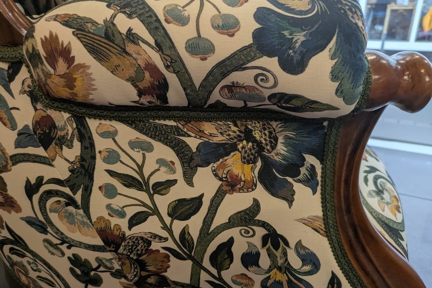 Nahaufnahme eines floralen Polsterstoffs mit Kordel und gedrechseltem Holzdetail an einem antiken Sofa
