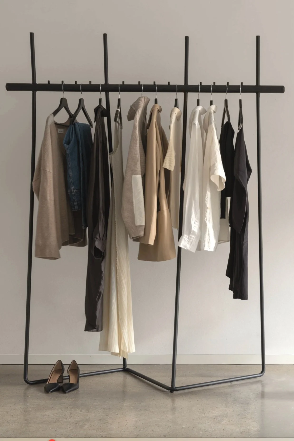 Nstyle.me - Clothing rack with beige, black, white, and gray garments and a pair of black shoes on the floor.