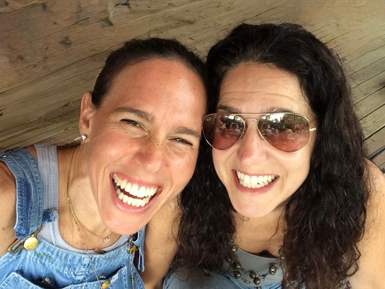 Two women smiling widely, one wearing sunglasses, captured from an overhead angle.