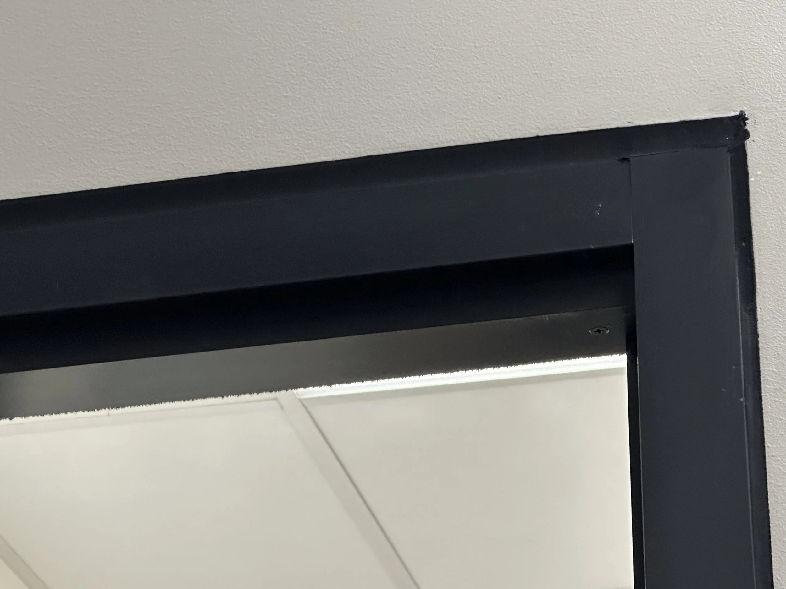 Close-up of a black door frame mounted on a textured beige wall, sealed with black caulking around the door perimeter.