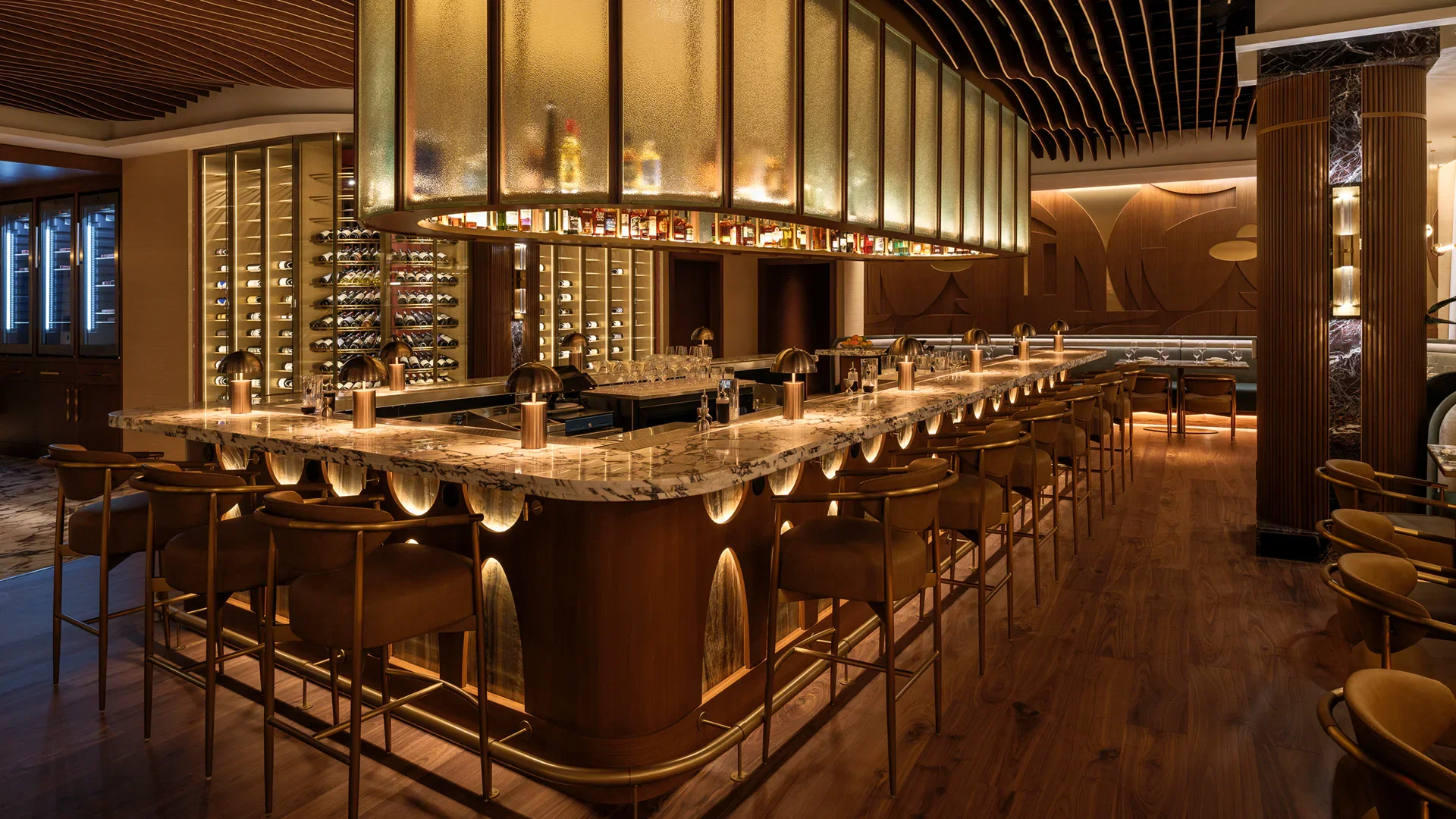 Elegant bar interior with marble counter, gold accents, wine display, and warm lighting.