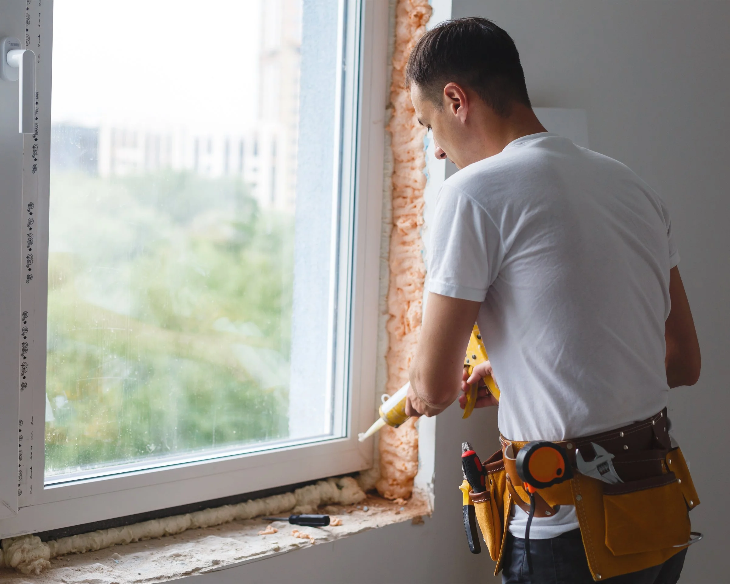 Contractor sealing a new window installation in a home.