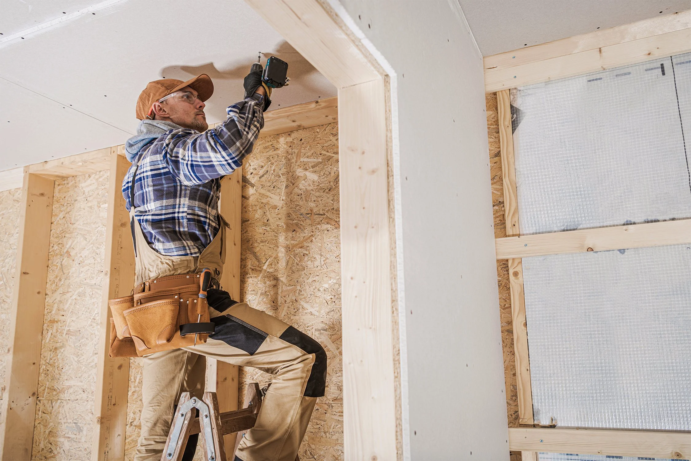 Construction worker installing drywall on a home's ceiling.