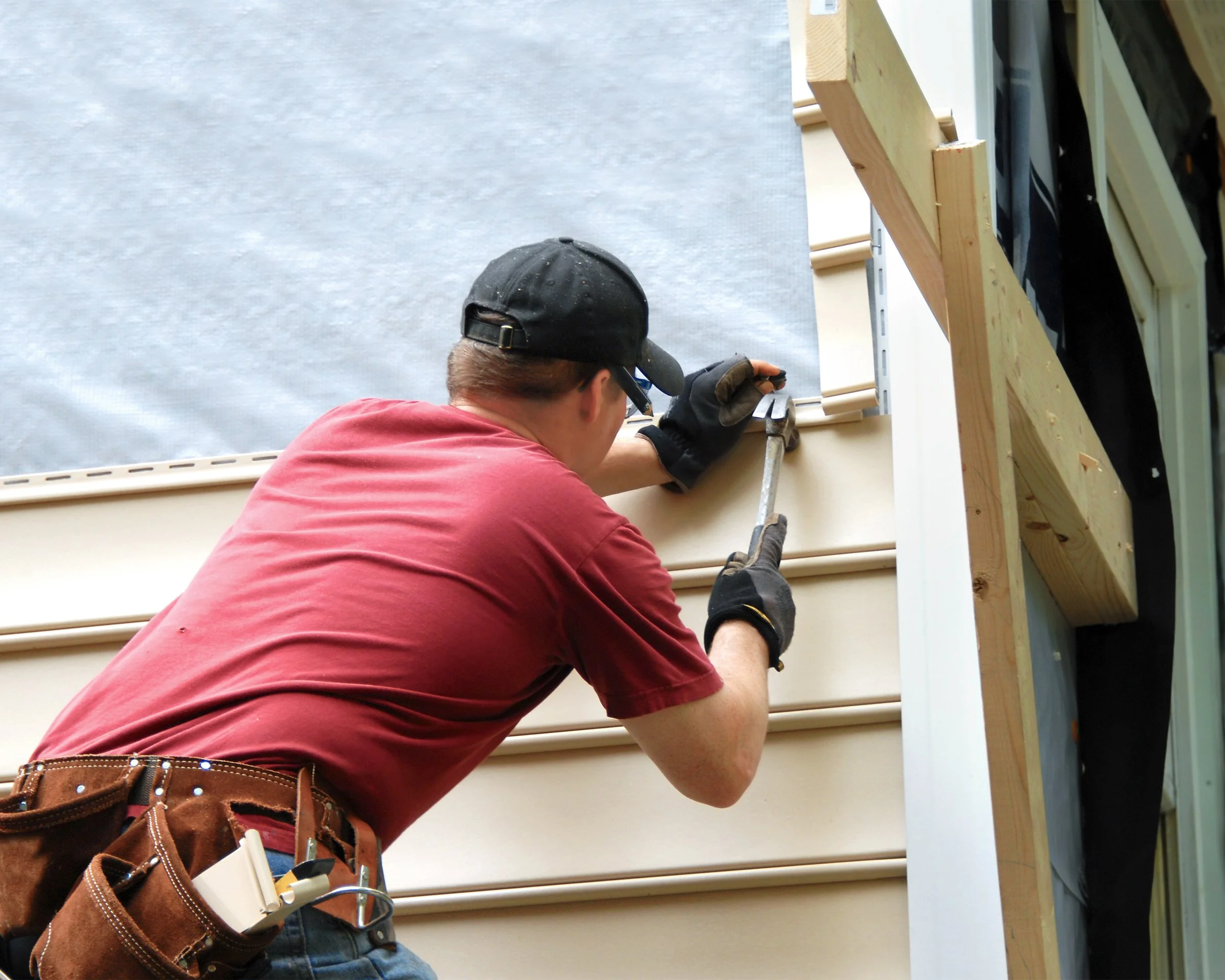 Contractor installing vinyl siding on a house.