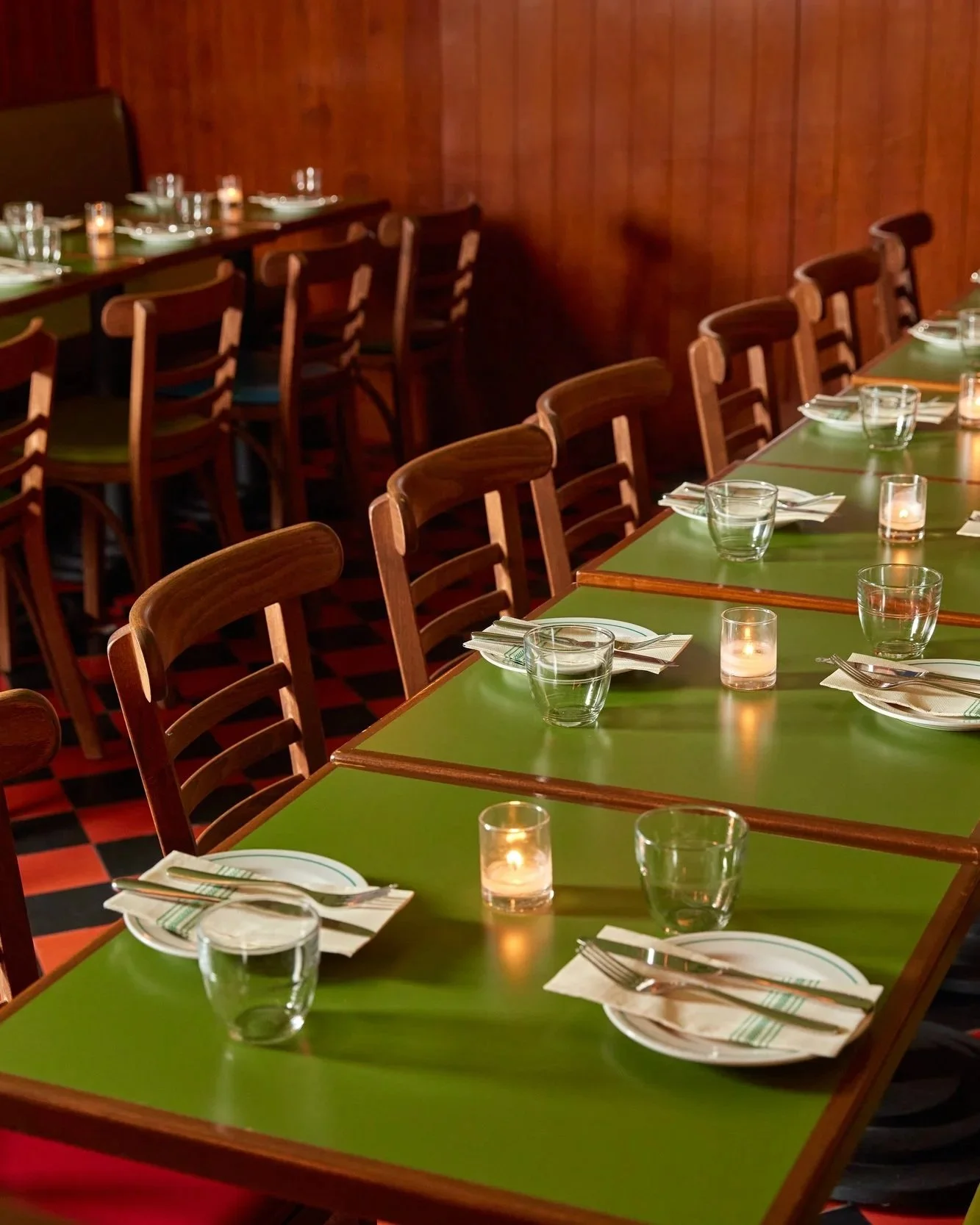 Restaurant table set with plates, utensils, water glasses, and lit candles in a cozy dining area with wooden walls and green tables.