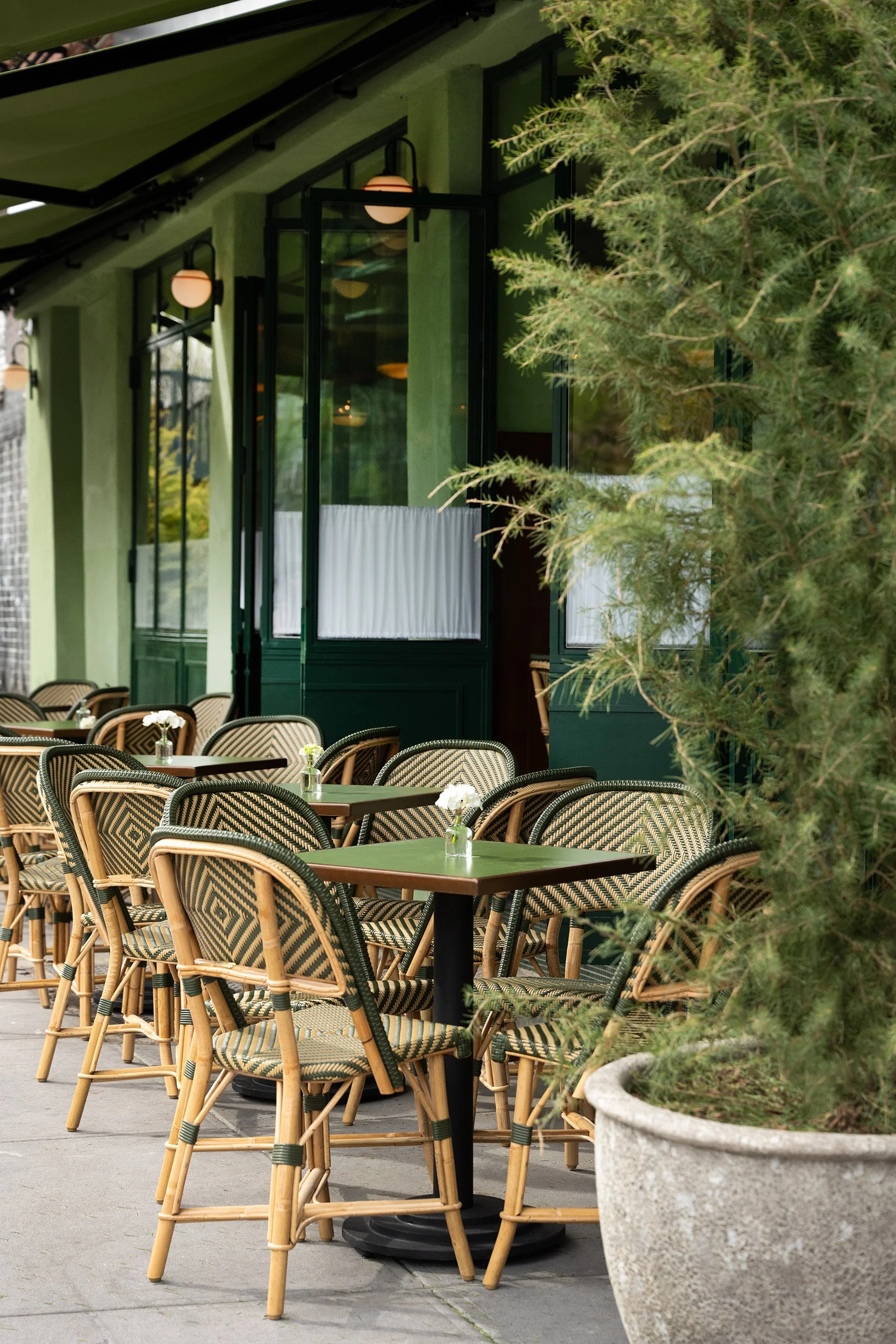 An exterior shot of Bar Bianchi in the daytime, french doors open with green toned two top tables and bistro chairs