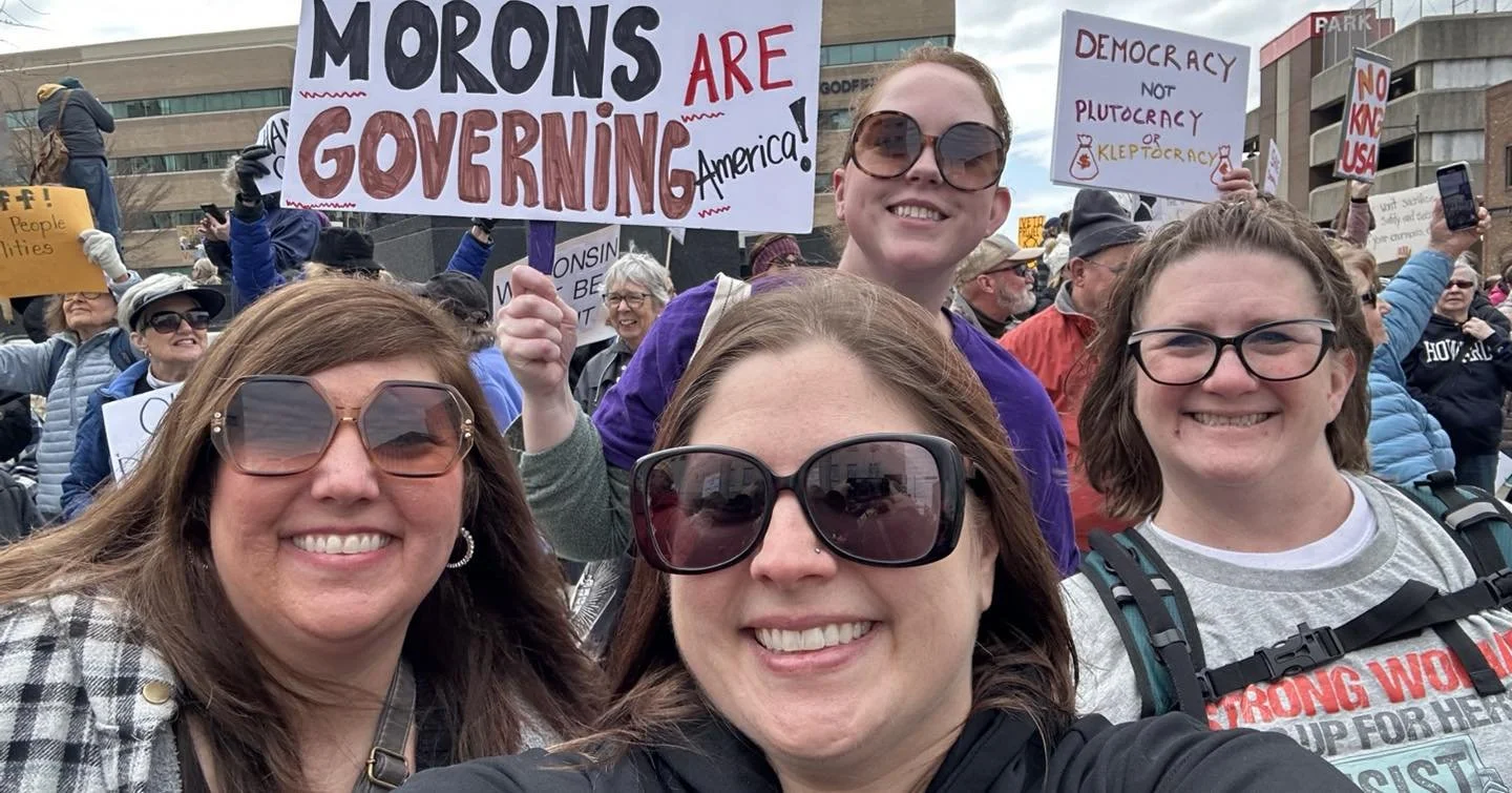 Group of people smiling at a protest, holding signs with political messages.