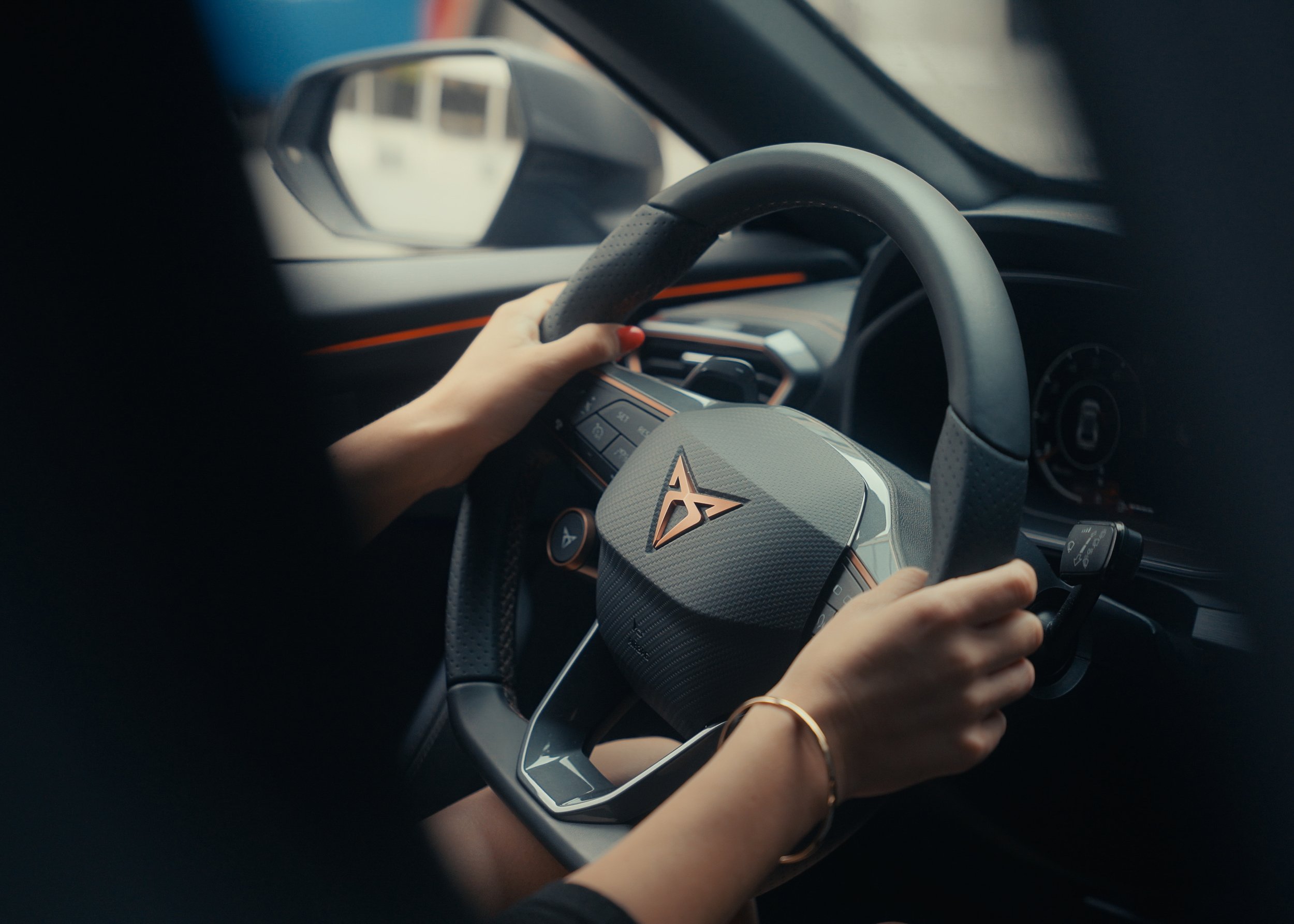 Person holding a steering wheel of a car, focusing on a stylish interior design and a visible emblem on the steering wheel.