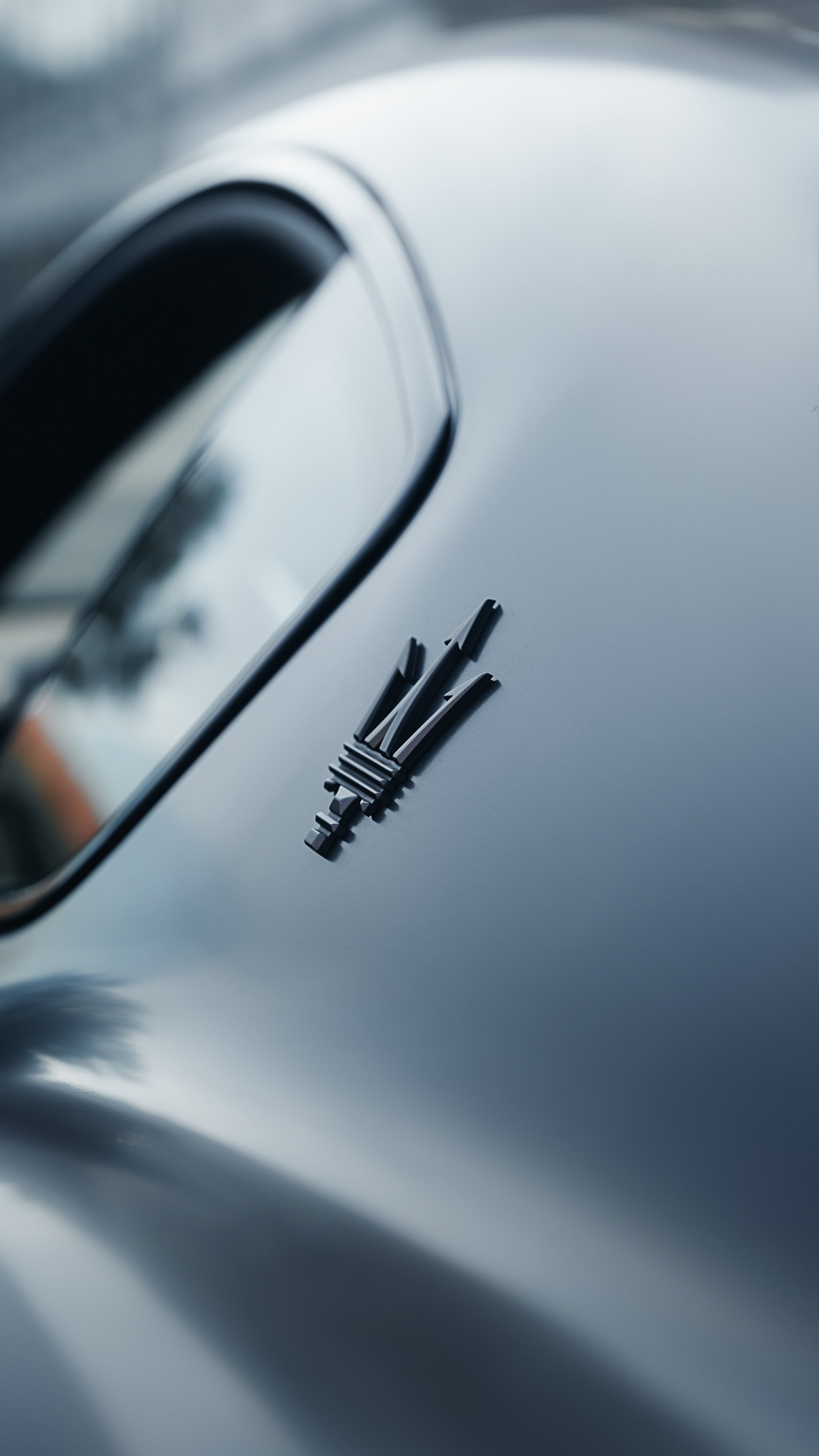 Close-up of a black trident logo on a silver car's surface with blurred background.