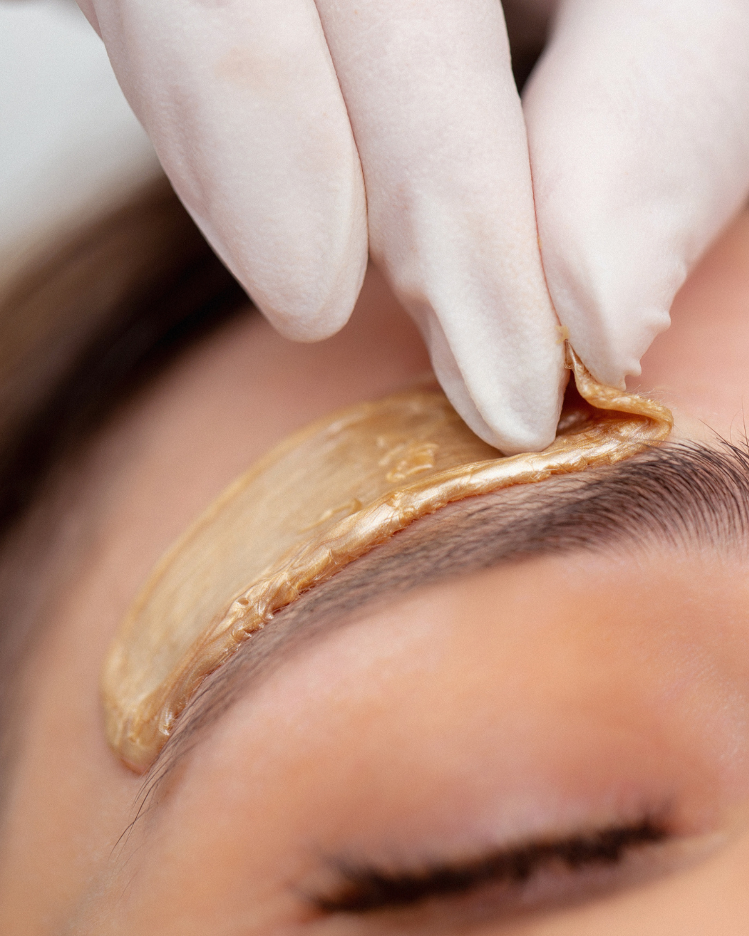 Close-up of a person receiving a facial treatment with a piece of adhesive or mask being applied around the eye area.