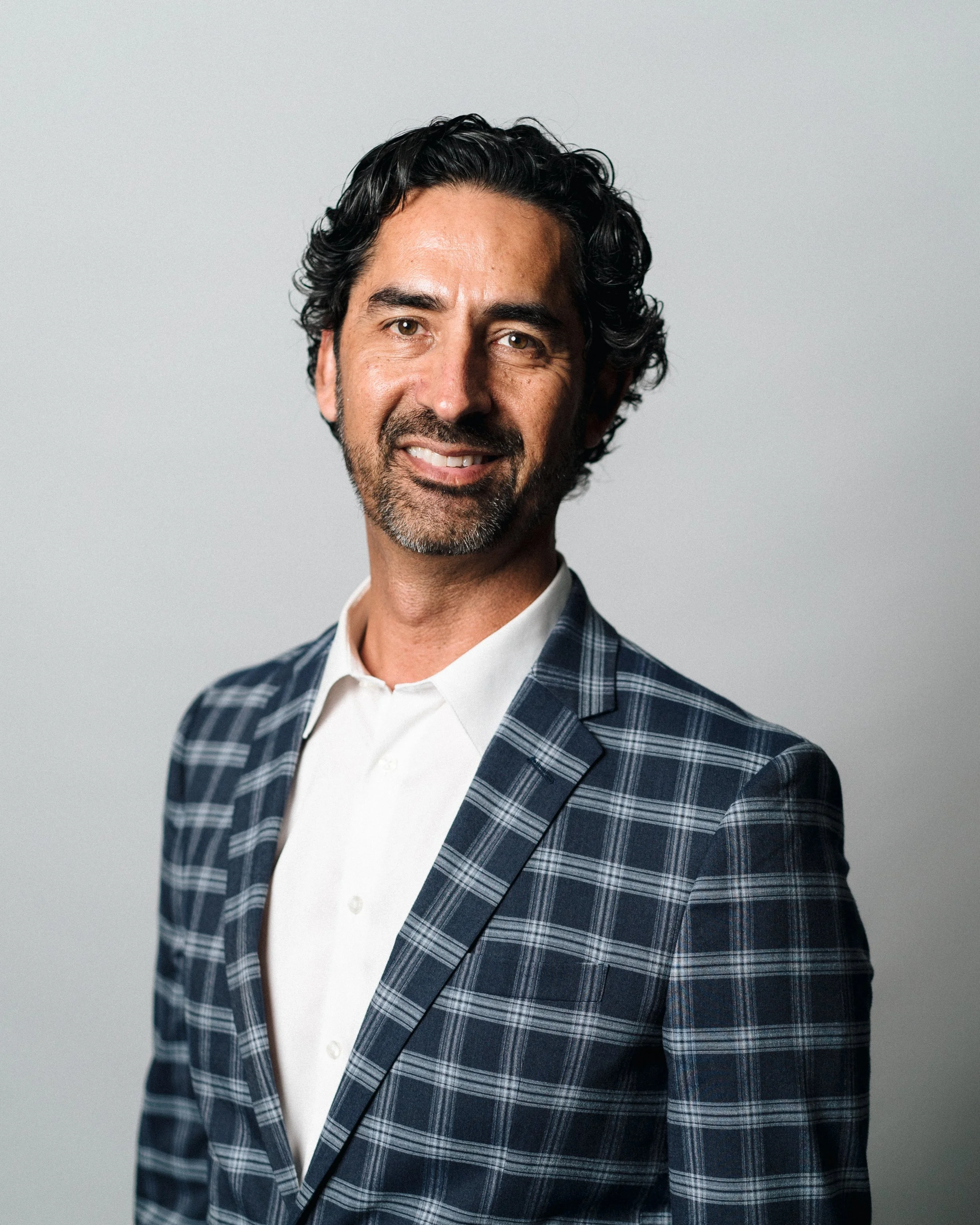 Smiling man in plaid suit jacket with white shirt in studio setting