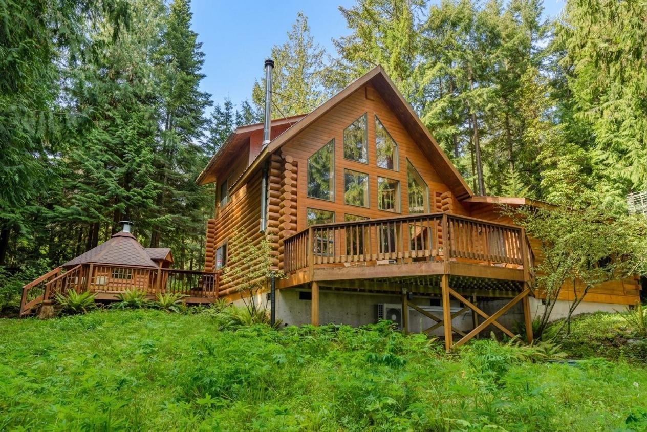 A large wooden cabin with multiple triangular and rectangular windows surrounded by lush green trees and grass.