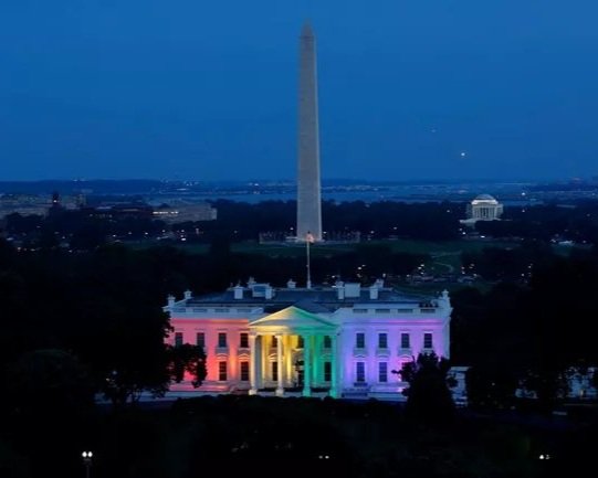 The White House lit up with rainbow colors at dusk, with the Washington Monument visible in the background.