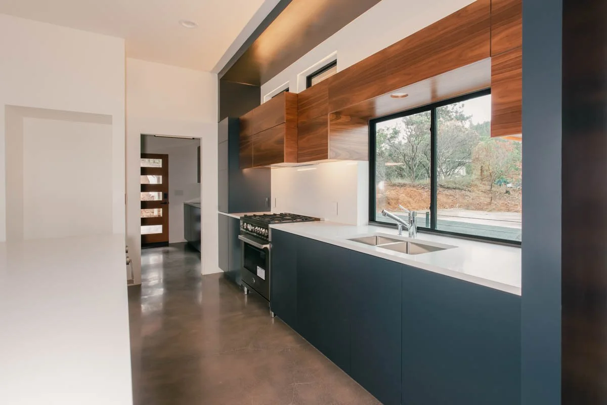 Custom kitchen with dark lower cabinets, wood upper cabinets, and picture window — built by Verity Construction in Southern Oregon.