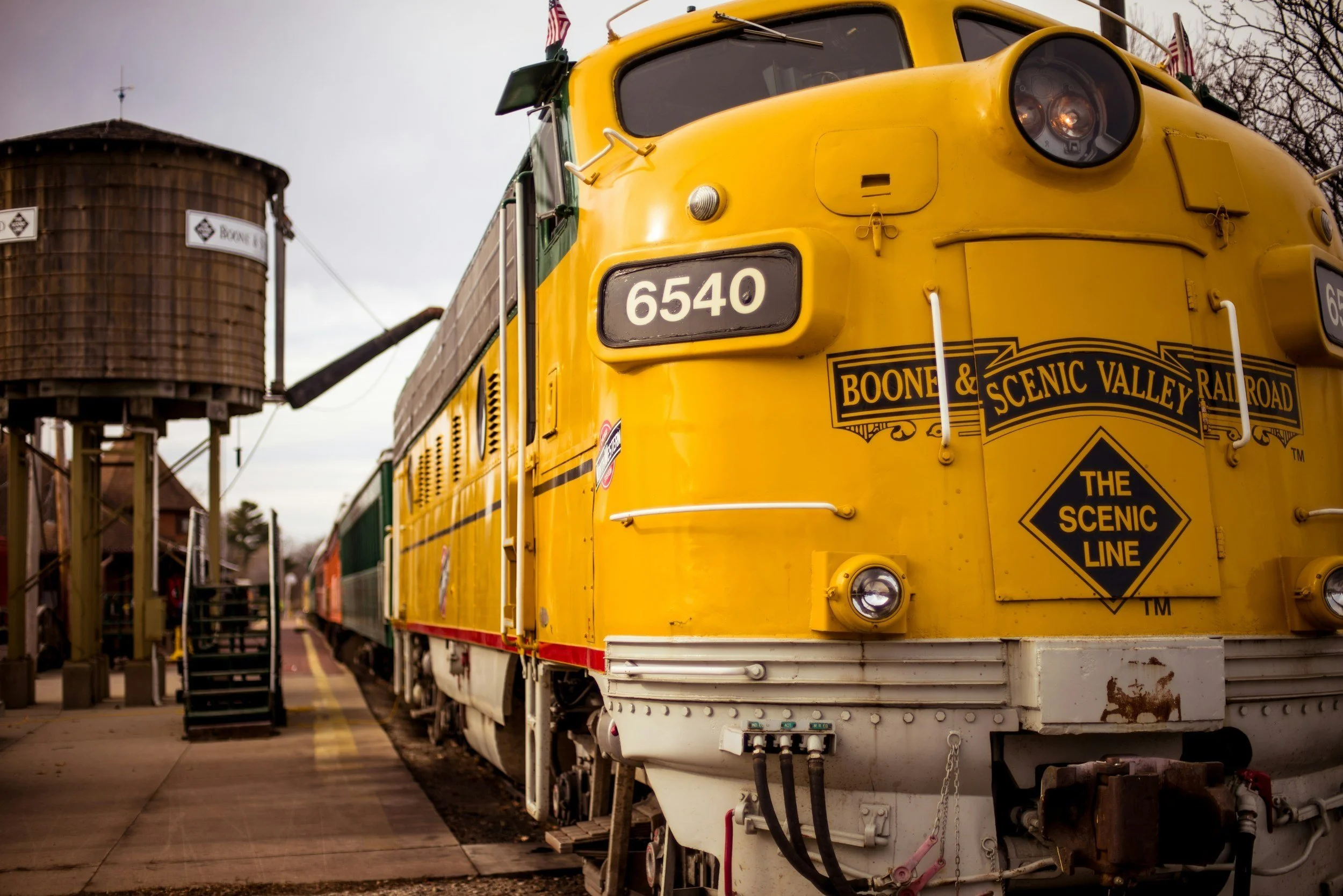 Yellow Boone & Scenic Valley Railroad train near a water tower.