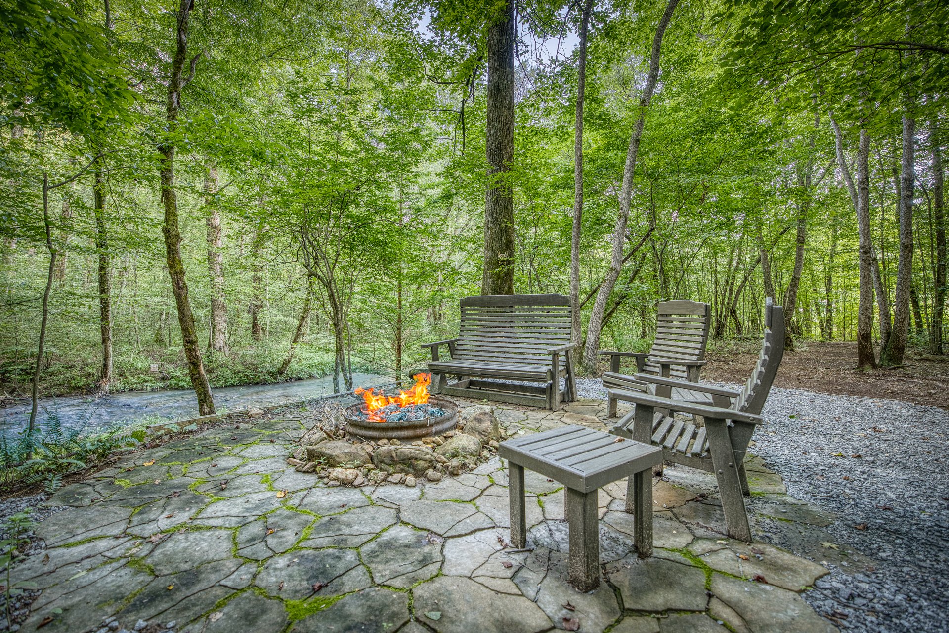 Peaceful creekside seating area with Adirondack chairs and a firepit, offering a serene spot to relax, unwind, and enjoy the sounds of flowing water and nature.