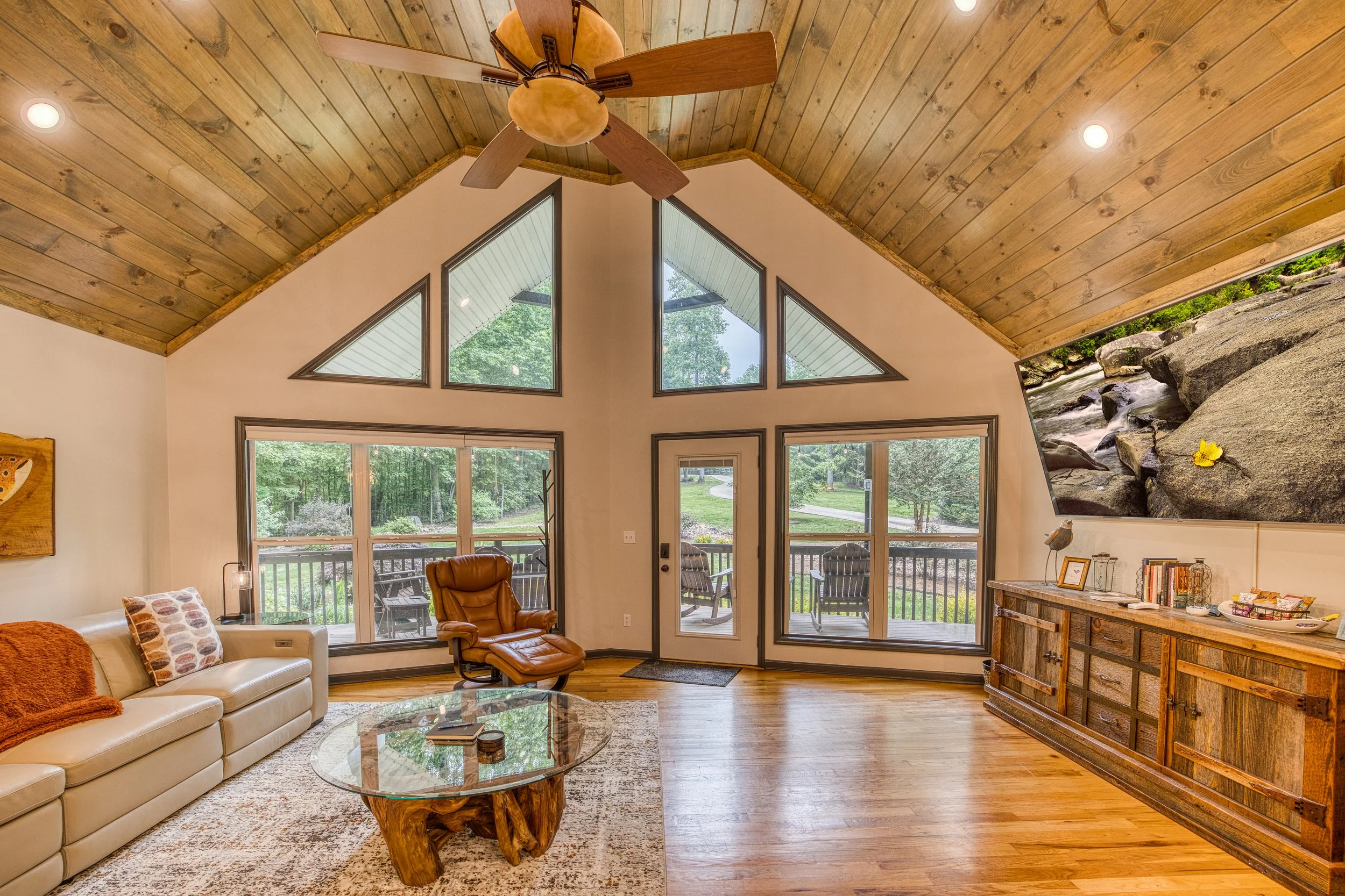 Vaulted ceiling living room with wall of windows, leather seating, and fenced yard views perfect for dogs.